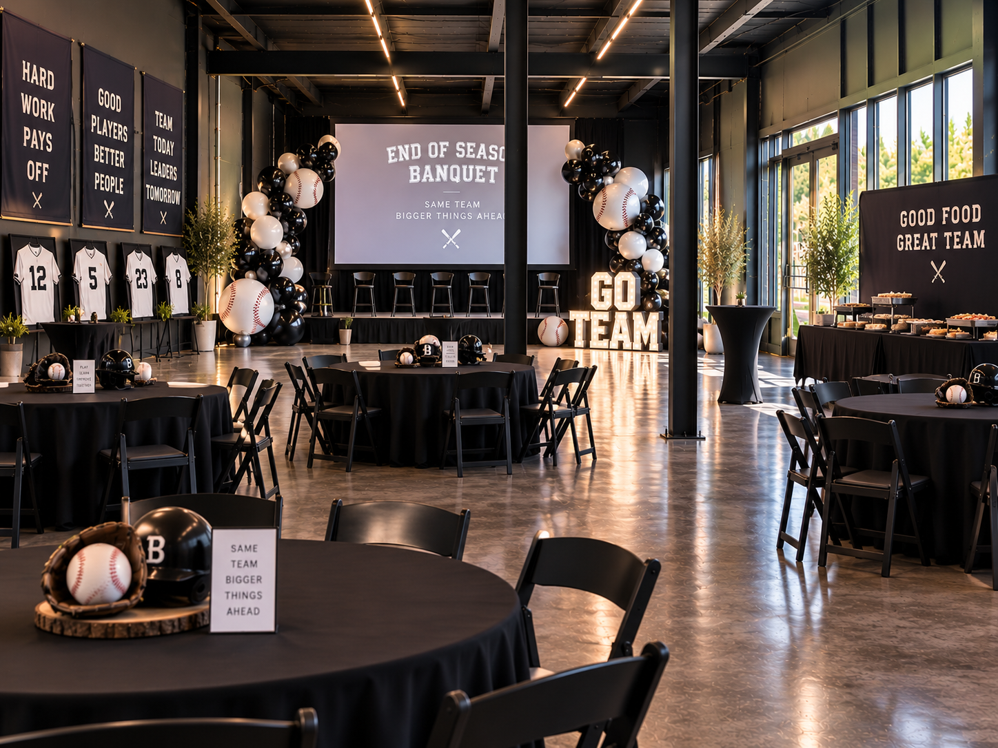 Indoor banquet setup with round tables, black linens, a big screen and balloon decor
